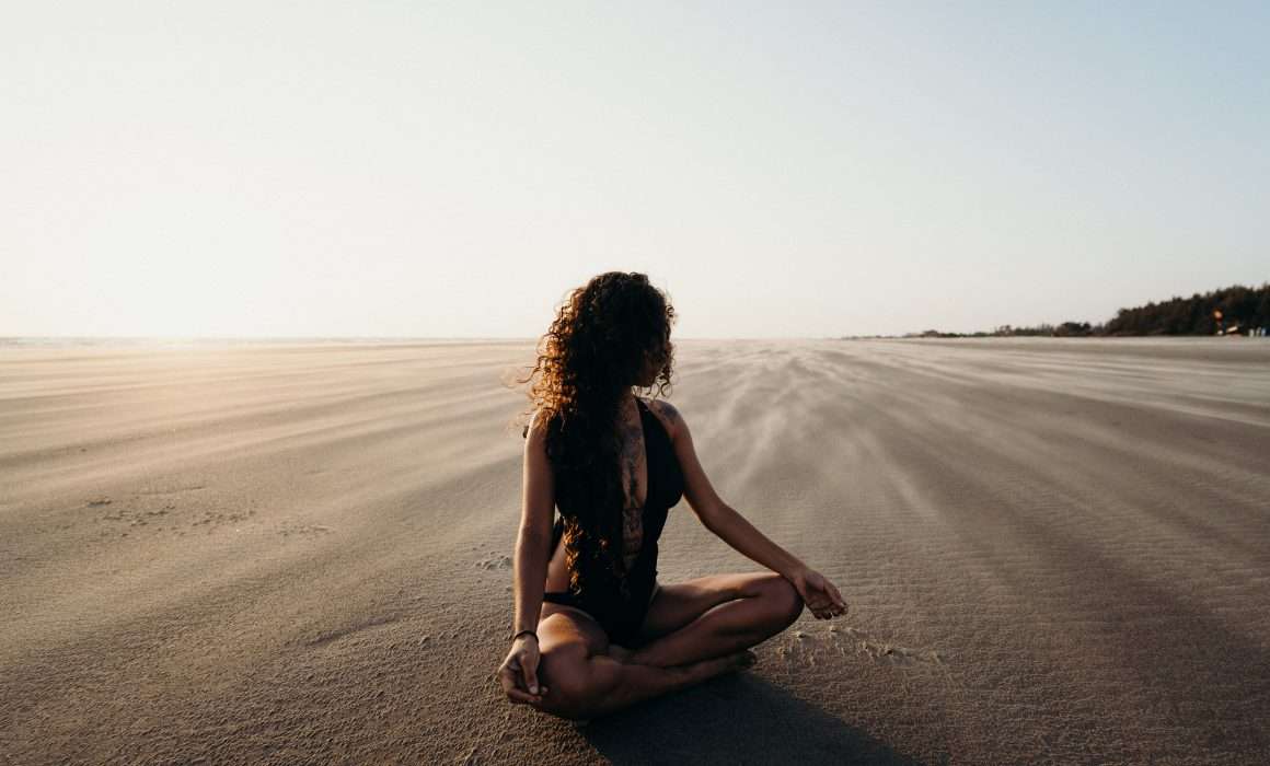 woman-sitting-on-sand-meditating