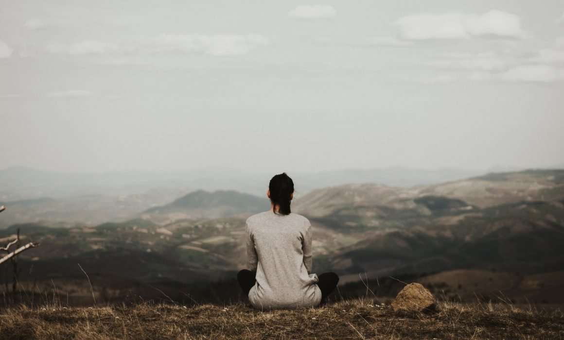 woman-sitting-on-hilltop-from-behind