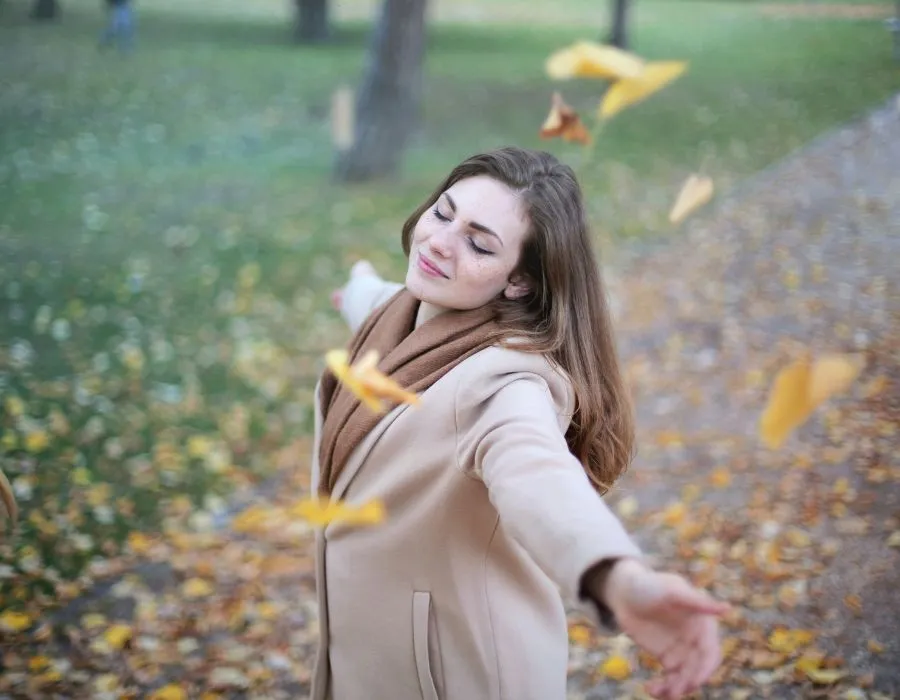 woman-in-park-winter-coat-leaves-falling-smiling-up-at-sky-eyes-closed-self-care-sunday-blog